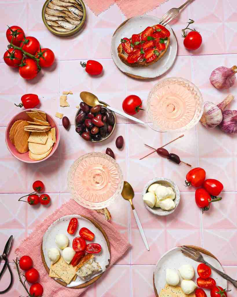 Flatlay of tomatoes, Bocconcini, olives, sardines on pink tiled backdrop