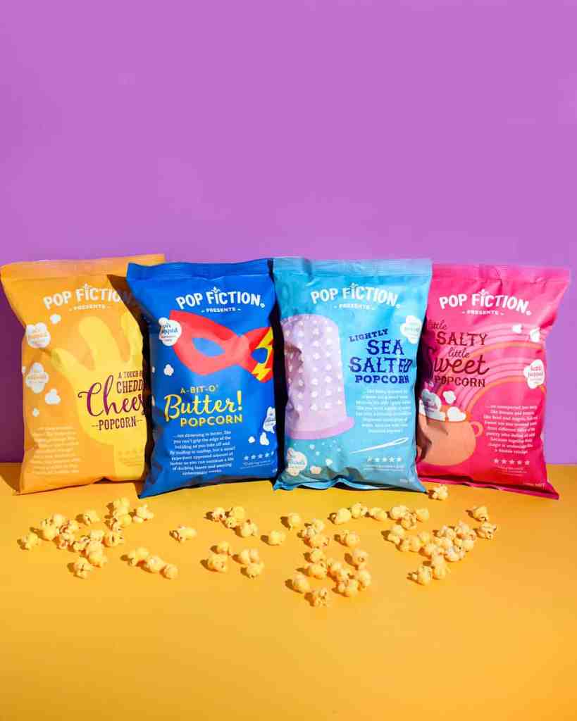A colourful selection of Popfiction popcorn bags standing up against purple backdrop on a yellow base